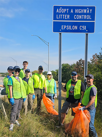 Epsilon C5I employes at an Adopt A Highway sign.