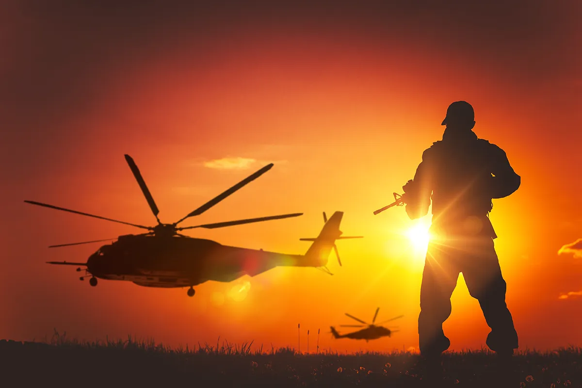 Soldier in front of two Blackhawk helicopters flying at sunset.